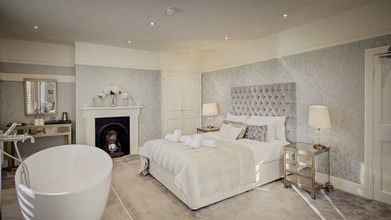 A bedroom suite at Vaulty Manor, with an upholstered headboard, freestanding bath, original fireplace and dressing table, set up for a wedding-night stay.