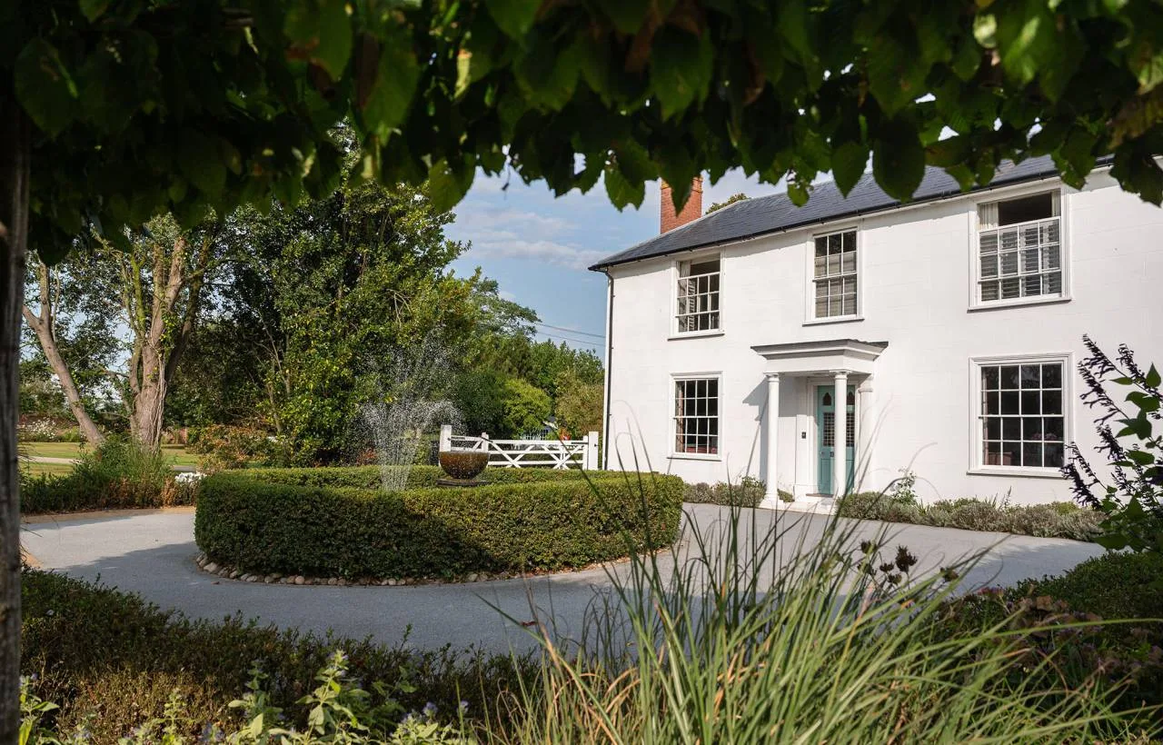 The Manor House at Vaulty Manor in summer, viewed across the front lawn with a fountain in the foreground and mature trees framing the white-painted Georgian facade.
