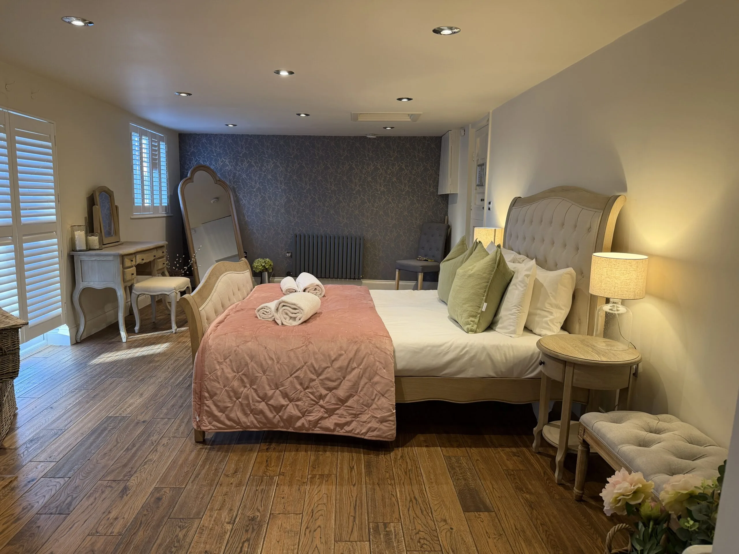 A bedroom in Rose Cottage at Vaulty Manor, with a dressing table, mirror and shuttered windows letting in soft morning light, set up for the bridal party to get ready.